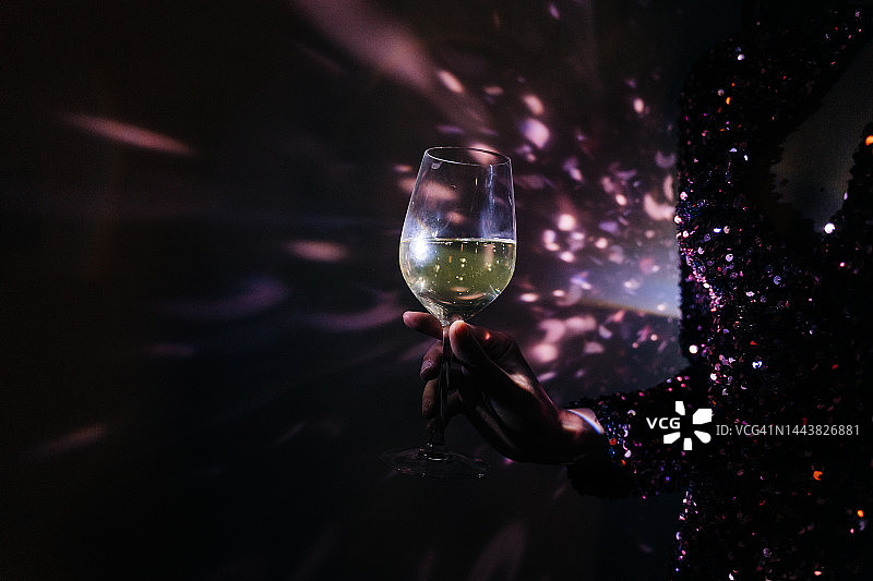 在黑暗迪斯科灯光下举着香槟酒杯的女人图片素材