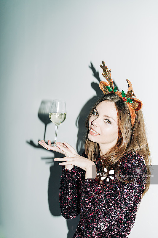 穿着闪光连衣裙，戴着香槟和驯鹿头带的年轻女人图片素材