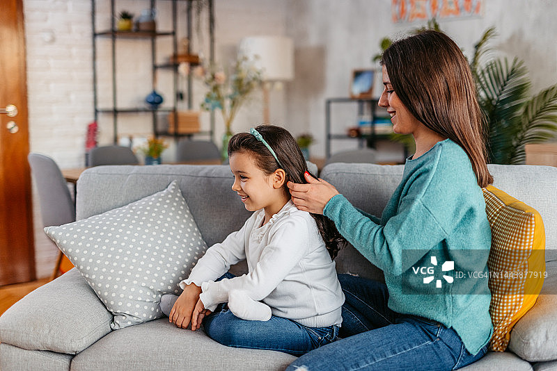 年轻的母亲在沙发上给女儿编头发图片素材