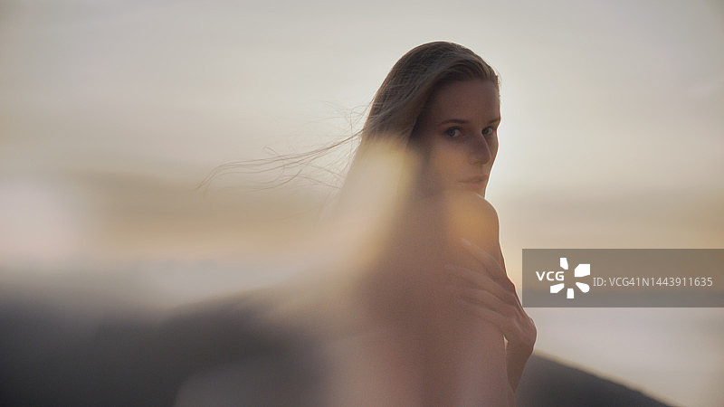 金色头发的美丽女神身穿白色长袍，沐浴在夕阳下，对着镜头微笑图片素材