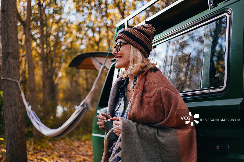 快乐的女人站在森林里她的面包车前，手里拿着一杯咖啡图片素材