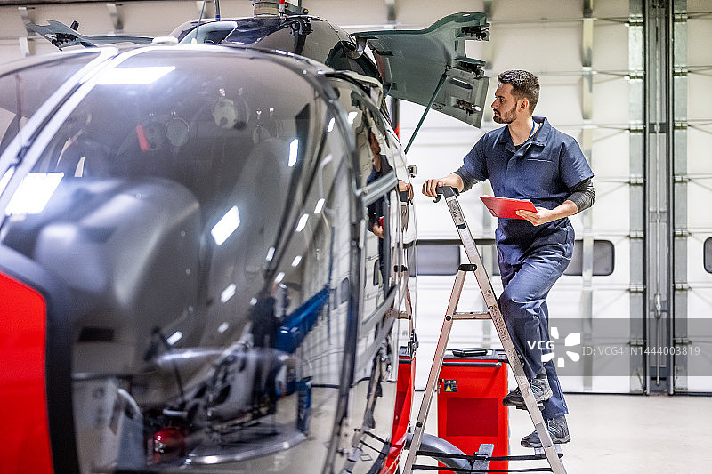 飞机修理工站在梯子上检查直升机侧面图片素材