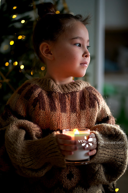 女孩穿着暖和的毛衣，在圣诞树背景下手持蜡烛图片素材