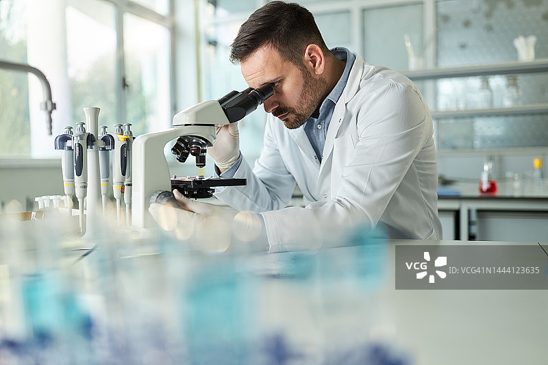 年轻男化学家在实验室用显微镜检查医学样本图片素材