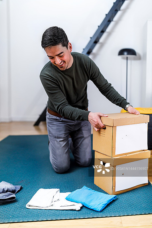 一位年轻男人正在将衣服装在纸箱里，准备做慈善捐赠图片素材