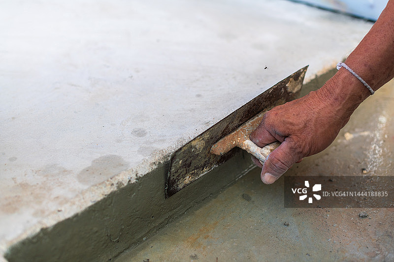 石膏匠正在使用不锈钢抹刀来粉刷抛光的本地水泥表面图片素材