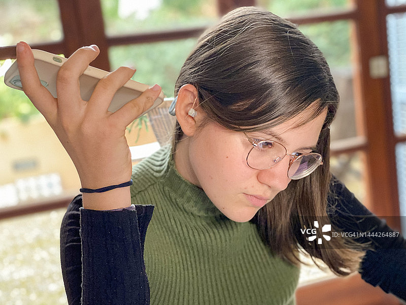 戴着助听器的少女在耳边用手机听信息图片素材