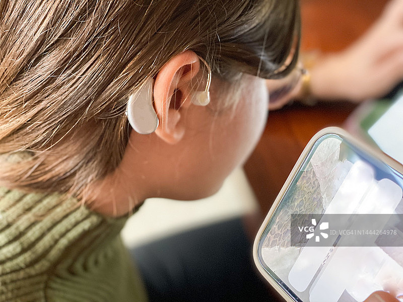 戴着助听器的少女在耳边用手机听信息图片素材