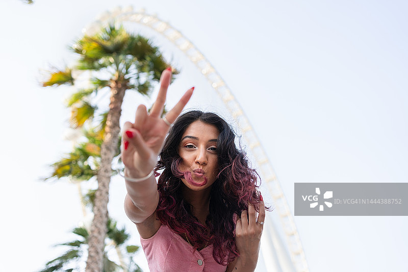 在摩天轮前展示和平手势的年轻女子图片素材