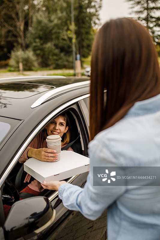 服务人员在汽车餐厅窗口向顾客递送咖啡和外卖披萨图片素材