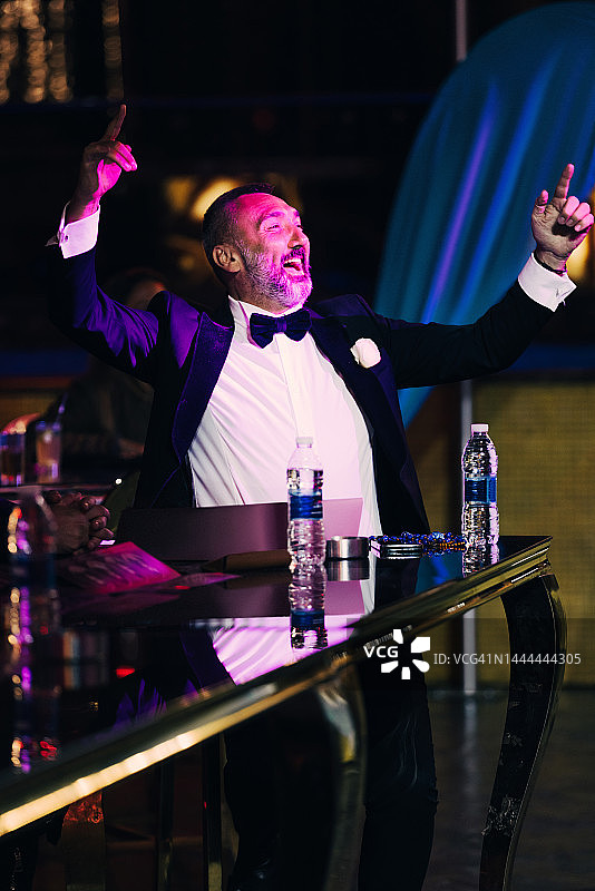 身穿黑色西装、系着蝴蝶结的成熟胡须男人坐在酒吧里，愉快地观看表演图片素材