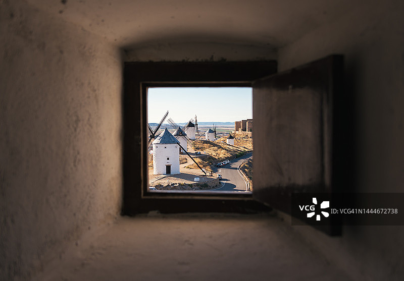 从磨坊内部窗口看到的西班牙典型白色风车和中世纪城堡图片素材