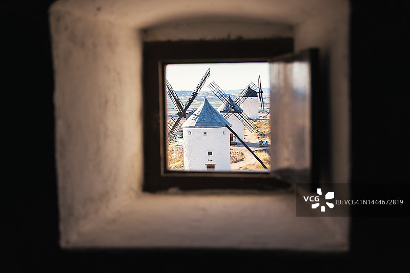 从磨坊内部窗口看到的西班牙典型白色风车和中世纪城堡图片素材