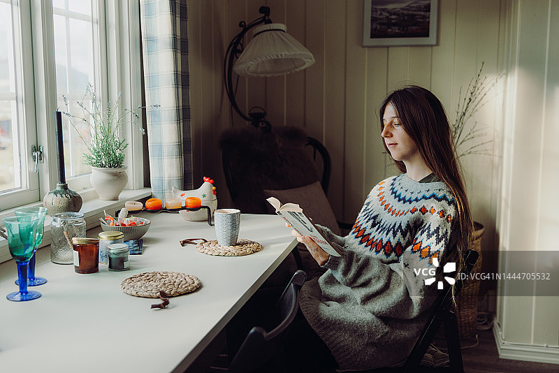 穿着羊毛毛衣的女人在家里舒适的早晨阅读书籍和喝咖啡图片素材