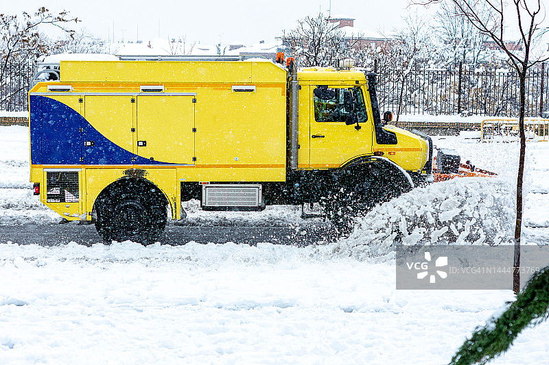 黄色扫雪机在城市的主要道路上清扫积雪的侧面图片素材