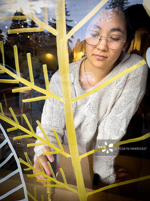 欧亚年轻女性在咖啡店的窗户上绘制圣诞树图片素材
