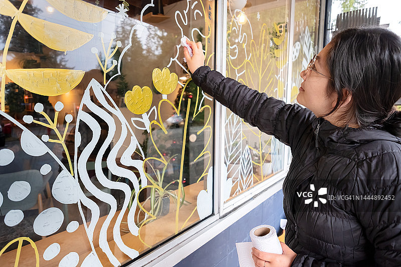 欧亚年轻女艺术家在画完冬季景色后清洁窗户图片素材