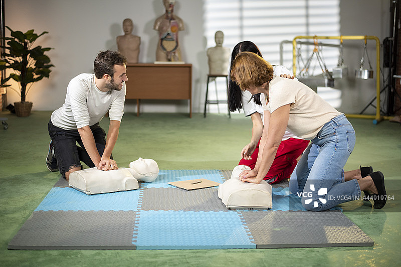 两人正在模拟人身上进行基础心肺复苏，教练在旁指导。图片素材