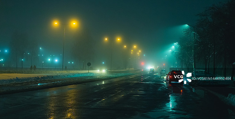 雾天夜雾：道路能见度低，车辆行驶，交通拥堵，湿滑的路面，车头灯，光线，道路上的冰雪，城市街道图片素材
