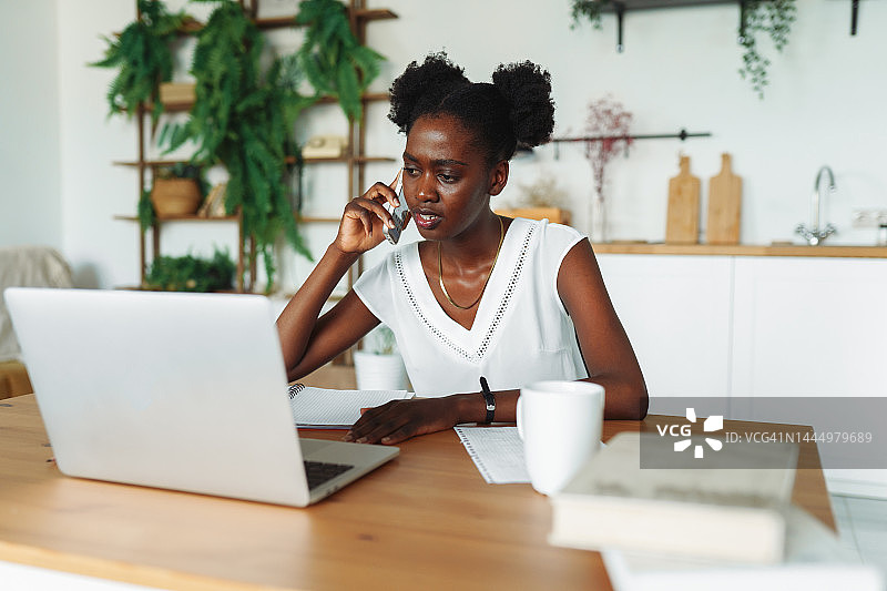 财务顾问远程办公，进行电话沟通和经济业务。 跨种族女人在家中使用笔记本电脑时，用智能手机拨打电话图片素材