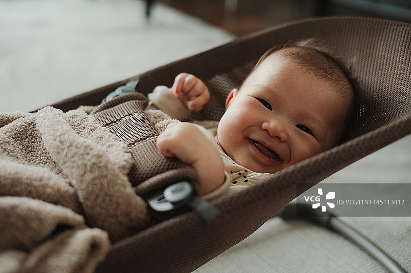 可爱的亚洲女宝宝躺在家中摇椅上，对着镜头微笑的肖像。婴儿期，美丽的宝宝笑容图片素材