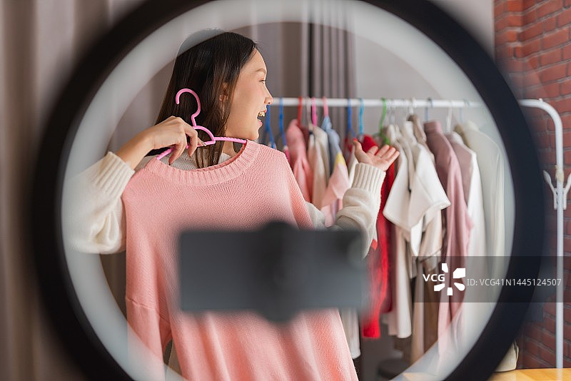 一位美丽的年轻亚洲女性小型在线企业经营者在社交媒体上进行直播，促销和销售她的打折服装的照片图片素材