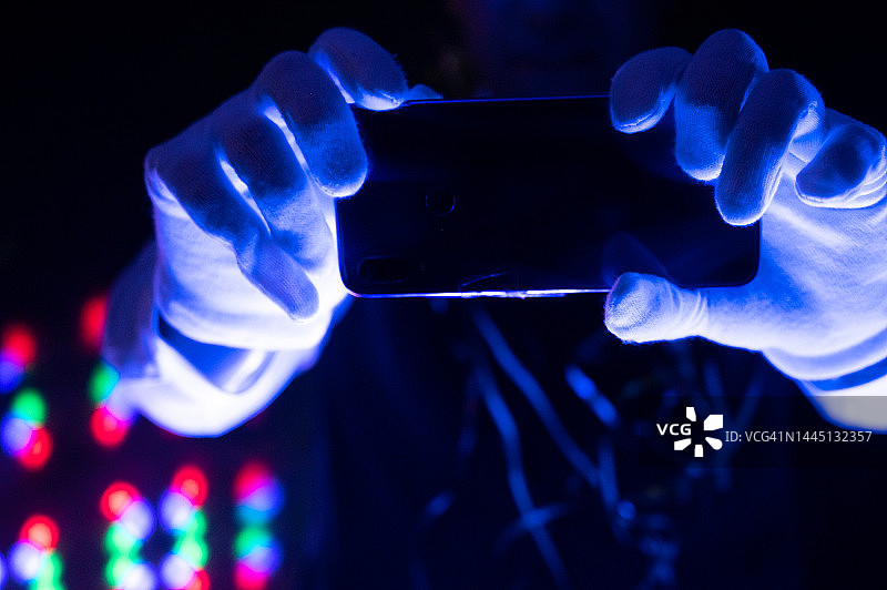 男子在迪斯科舞厅跳电音，用智能手机拍照，紫外线照明图片素材