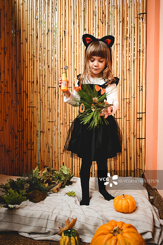 穿着橙黑色女巫服装，站在南瓜旁边的可爱小女孩图片素材