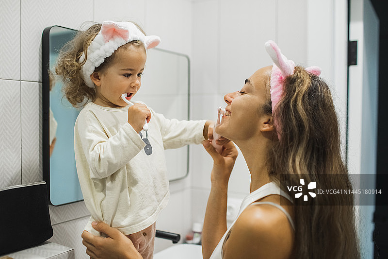 年轻母亲和女儿一起刷牙，宝宝笑着很开心图片素材