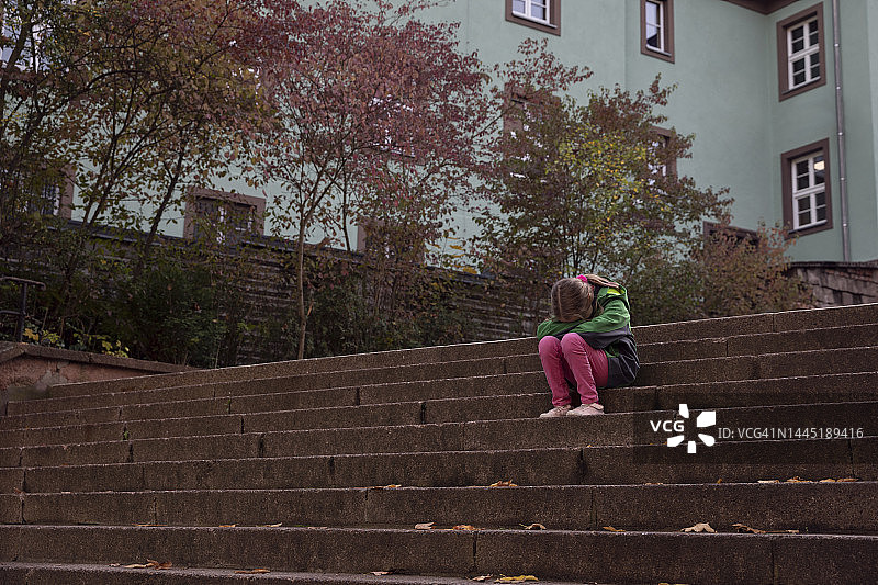 独自坐在小镇宽阔石阶上的9-10岁儿童，头放在膝盖上，传达出绝望和孤独感。图片素材