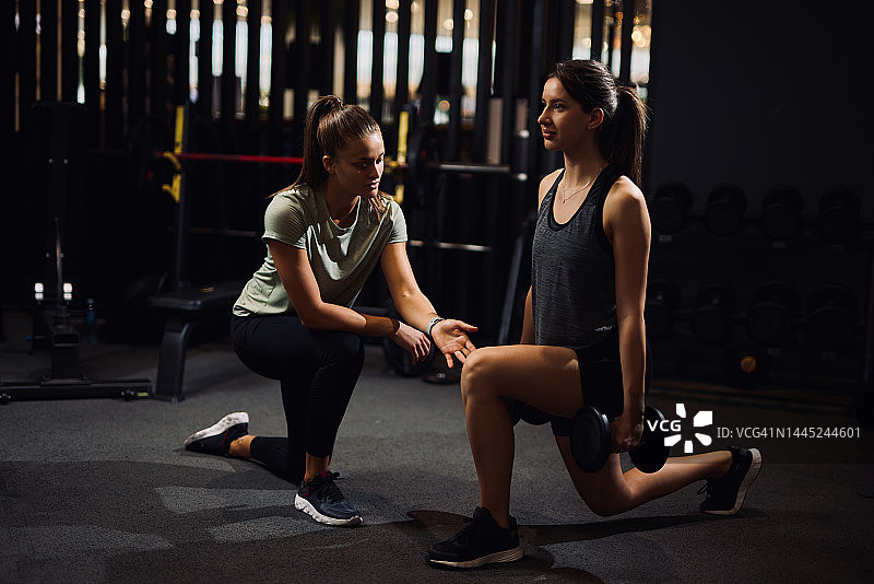 私人教练指导女人在现代健身房做哑铃深蹲图片素材