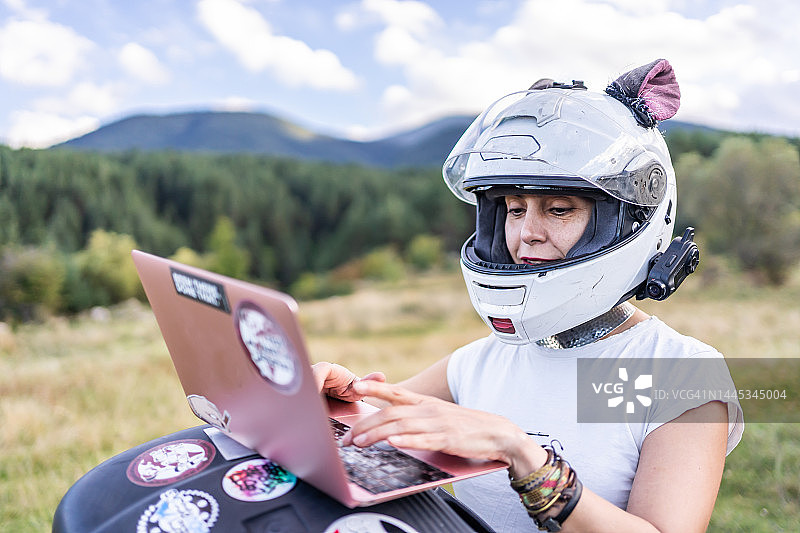 女人站在森林里的摩托车旁使用笔记本电脑图片素材