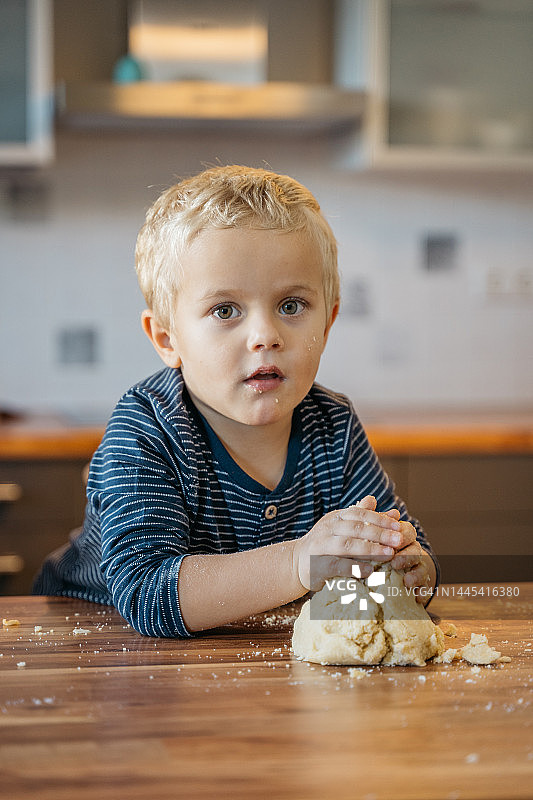 男孩靠在厨房柜台上揉捏饼干面团图片素材
