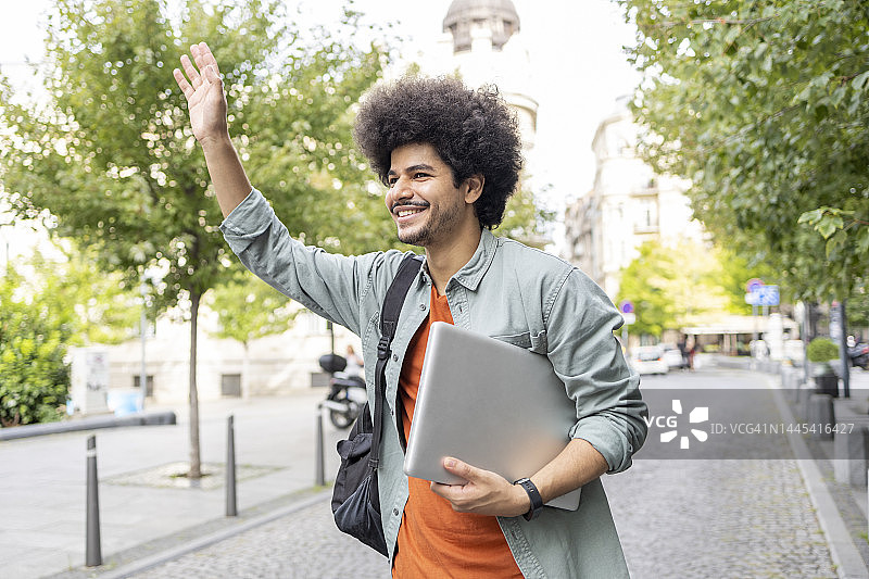 在街上招出租车的背着背包的微笑年轻人图片素材