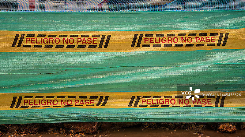 建筑工地周围塑料纺织屏幕上的西班牙语警告标志，写着“危险，请勿通行”图片素材