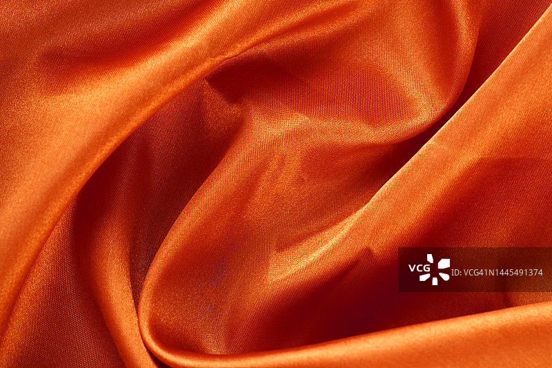 金色橙色缎面纹理背景，带波浪和褶皱。用于奢侈品展示的暖黄色布料背景。平铺，特写图片素材