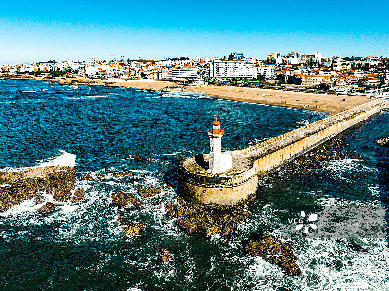 阳光明媚的日子里，波尔图费尔盖拉斯灯塔与海浪和城市景观的无人机视角图片素材