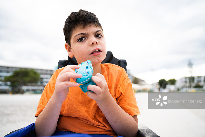 坐在轮椅上、手持玩具的残疾儿童在日落时分的沙滩上看着镜头图片素材