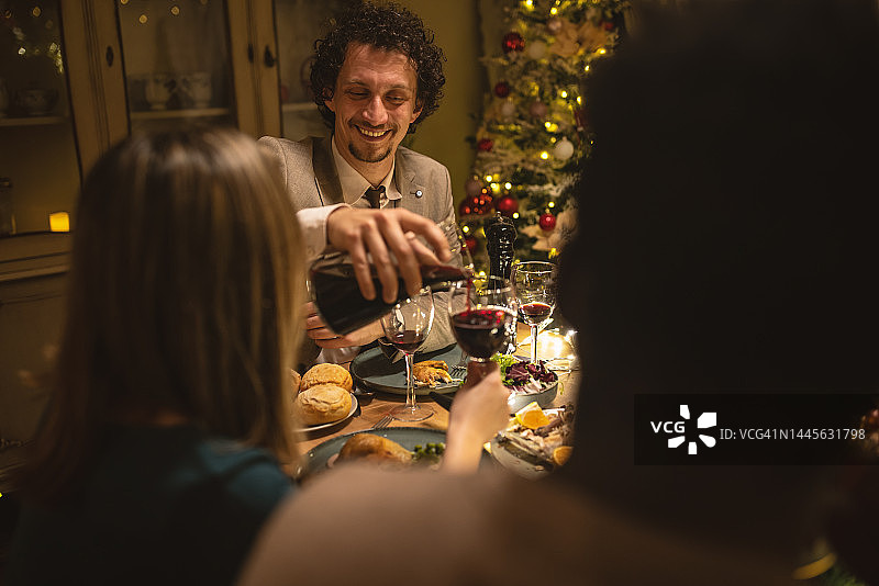 男人在圣诞晚餐给朋友倒酒图片素材