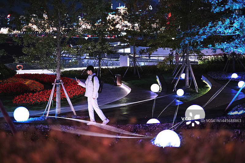 在公园里用智能手机控制灯光的亚洲男人图片素材