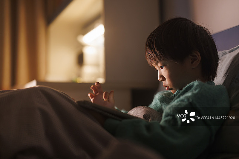 亚洲男孩睡前玩平板电脑图片素材