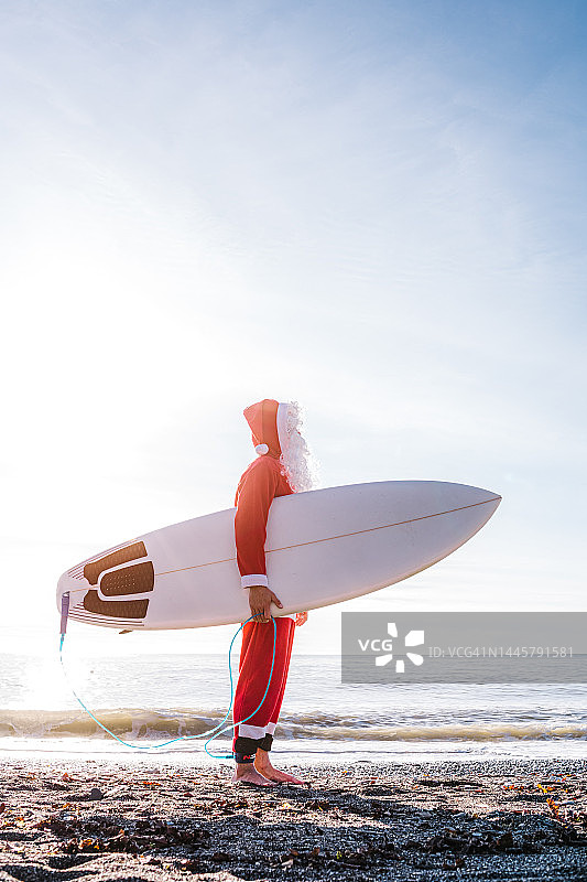 穿着圣诞老人服装，带着冲浪板在海滩上的冲浪者图片素材