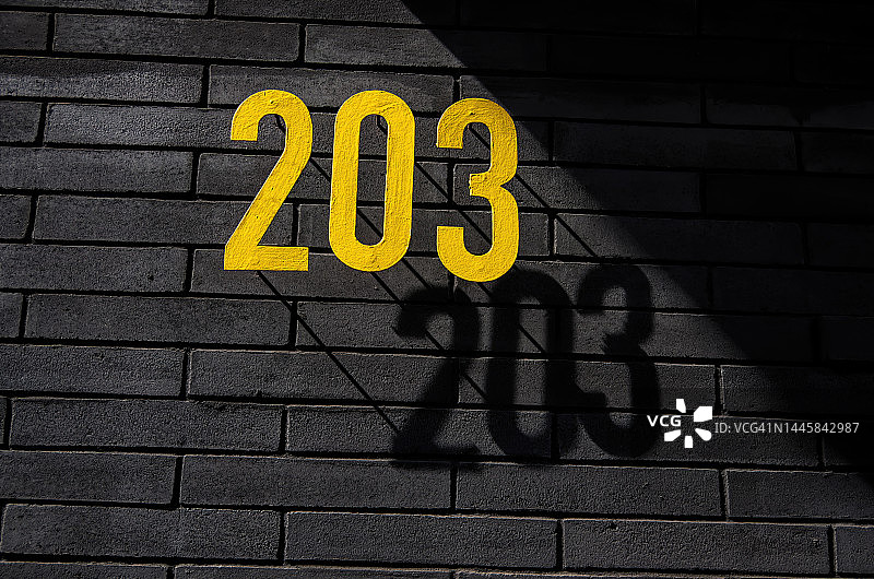 黑色砖墙上的黄色金属街道号码203图片素材
