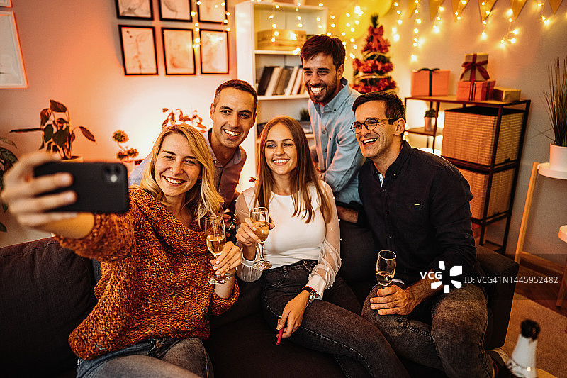 在家享用圣诞晚餐并用智能手机自拍的多元化朋友和家人图片素材