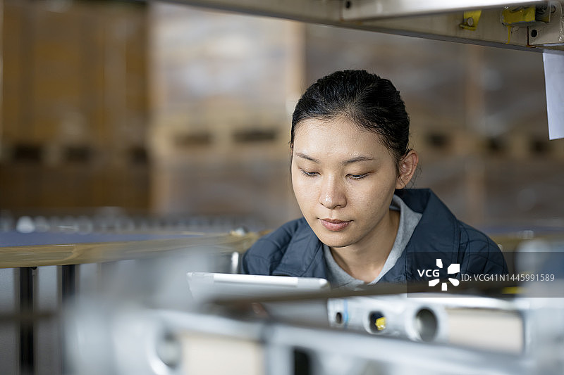汽车行业的仓库和供应链管理解决方案，亚洲仓库员工使用平板电脑清点工厂仓库中生产线的汽车零件库存图片素材