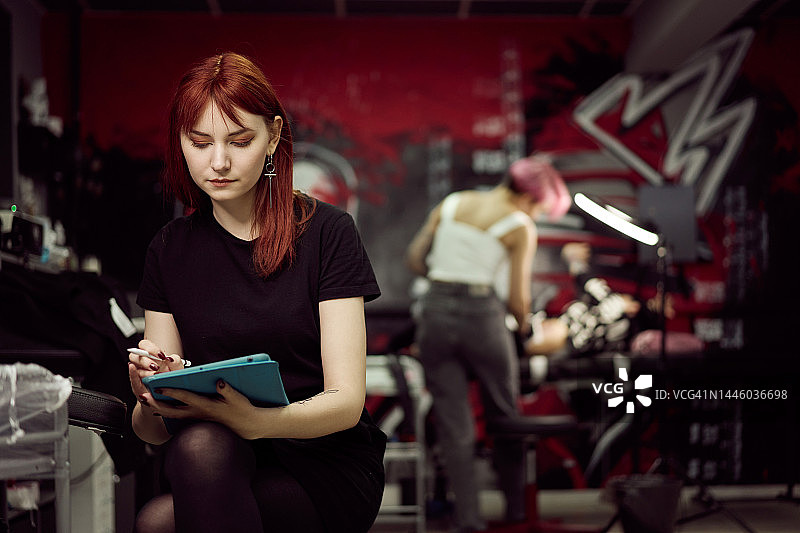 在工作室的笔式平板电脑上绘制纹身的姜黄色头发的女人图片素材
