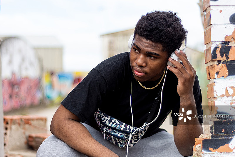 戴白色耳机听音乐的年轻黑人男孩，废弃建筑背景图片素材