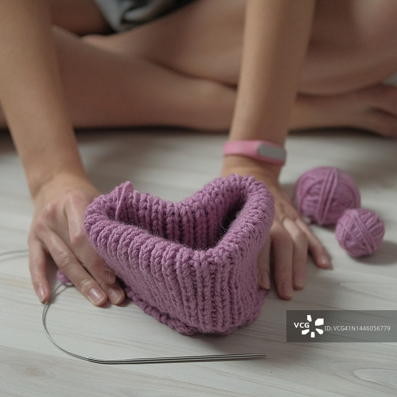 女孩在地板上手持毛线针编织的精美羊毛帽子图片素材