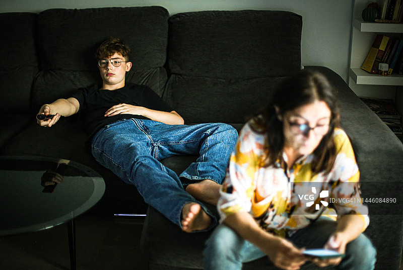 母子在沙发上放松地看电视和使用智能手机图片素材