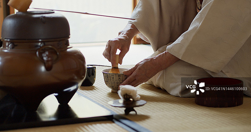 日本传统茶道的主持人正在搅拌茶水并奉上茶碗图片素材